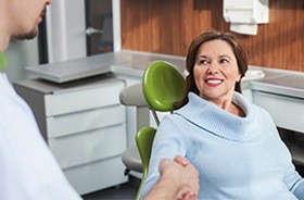 Woman in dental chair shaking hands with dentist