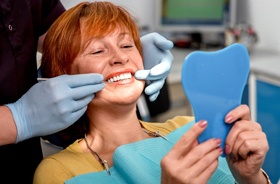 Happy patient looking in mirror, admiring her new dentures