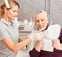 Mature male dental patient, holding mirror and admiring his smile