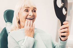 Dental patient using mirror to admire her new dentures in Plymouth
