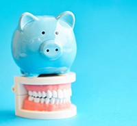 Blue piggy bank atop model teeth with blue background