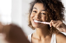 Young woman standing in front of mirror, brushing teeth