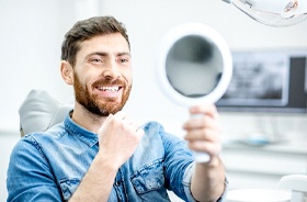 Man holding mirror, admiring his new dental implant restorations