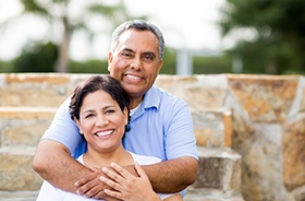 Smiling couple with dental implants in Plymouth standing outside