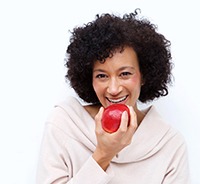 Woman with dental implants in Plymouth eating an apple