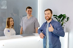 Man at dental office front desk, making thumbs-up gesture