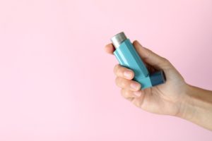 Hand holding inhaler for asthma in Plymouth against pink background