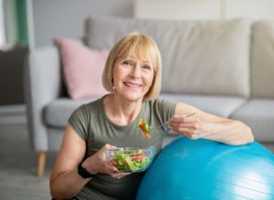 Senior woman enjoying salad with help of implant dentures in Plymouth